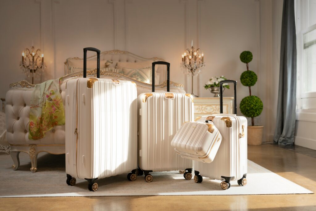 Luxury white and gold hardshell luggage set standing on a Persian rug in an opulent hotel bedroom, representing high-end travel aesthetics for couples.
