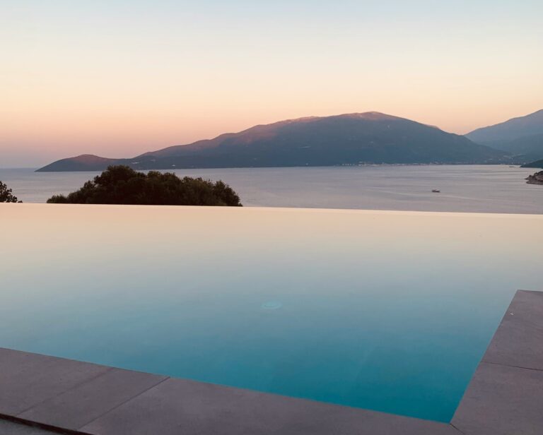 Piscina infinita branca e minimalista com vista para o Mar Egeu e a Caldera de Santorini, exemplificando a vibe Sun Chasers e hotéis boutique românticos na Grécia.