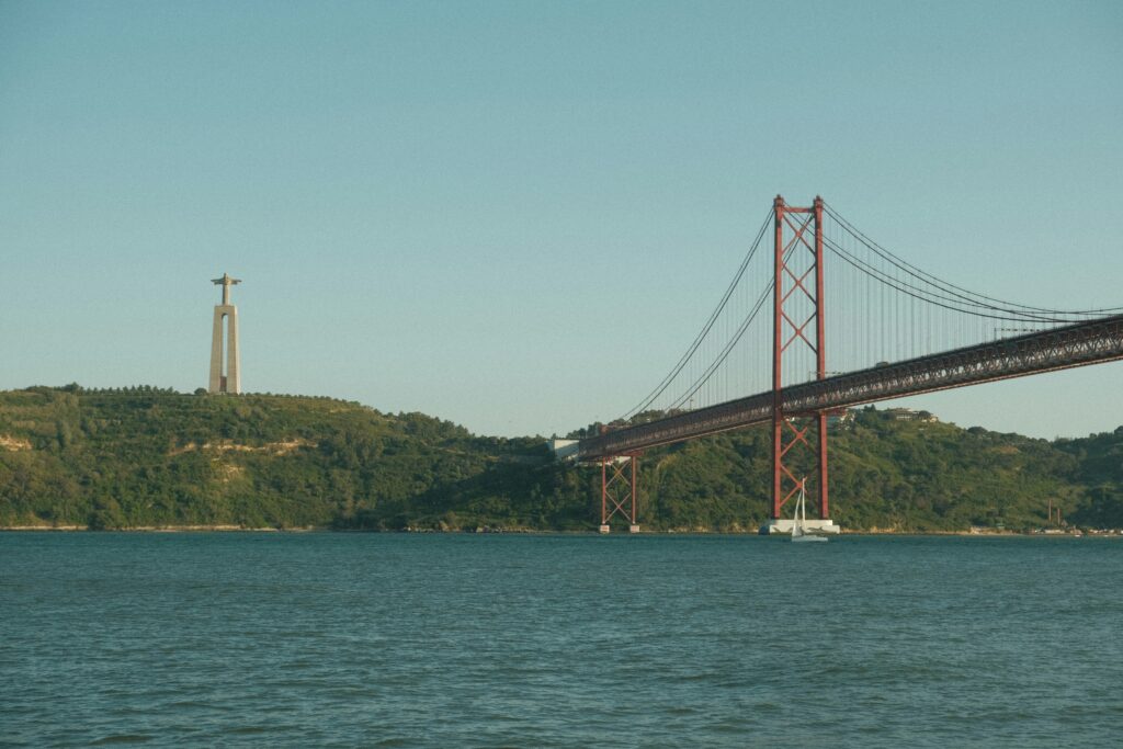 A sailboat gliding under the 25 de Abril Bridge during a Lisbon river cruise.