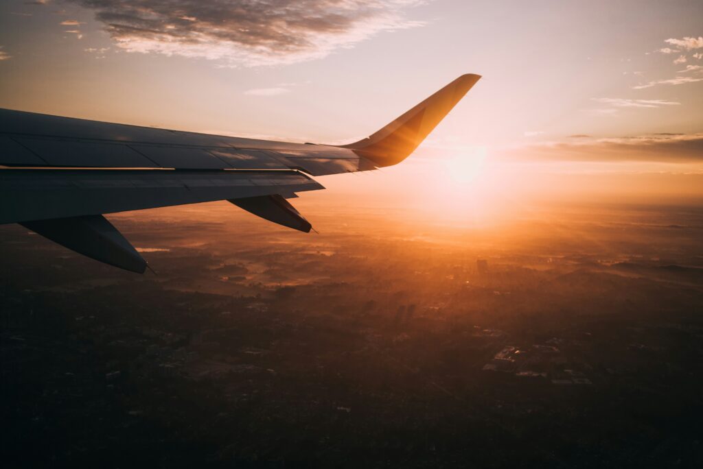 Airplane wing flying over mountains during a golden sunset, representing a luxury couple trip to Europe.